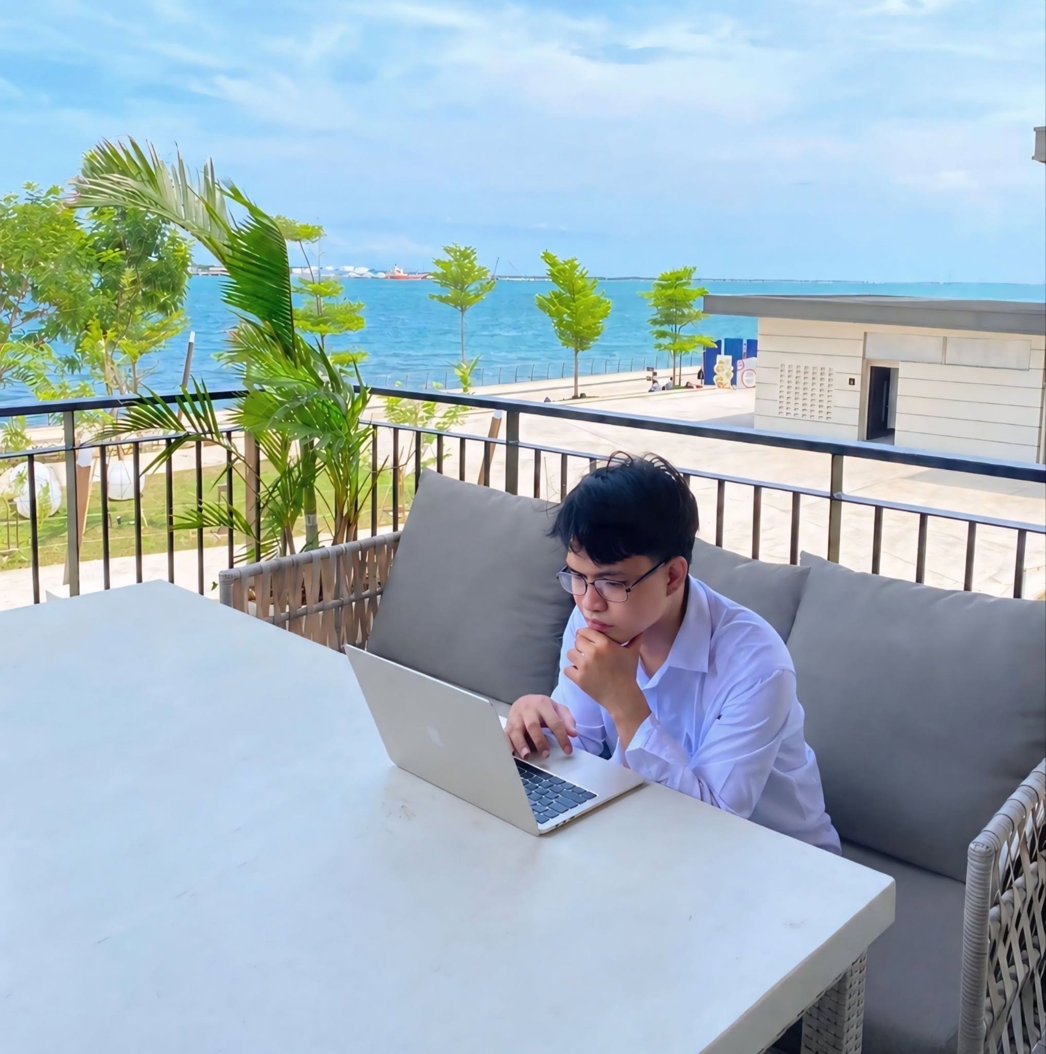 Francis Dela Cruz working on a laptop beside the sea
